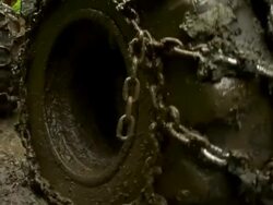 Close up of chained wheels of skidder as it moves through the mud away from the camera. Stock Footage