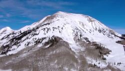 Snow clings to mountainsides and peaks rising against a blue sky. Stock Footage