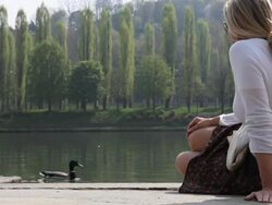 Woman watches ducks at river's edge, spingtime Stock Footage
