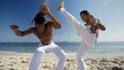 Brazilian capoeira martial artist kicks over opponent on beach in slow motion Stock Footage