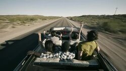 Friends driving through desert in red convertible throw arms in the air Stock Footage