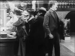 B/W 1916 Charlie Chaplin putting hands on counter + back kicking man (Albert Austin) in dept. store Stock Footage