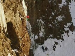 WS PAN View of ice climber going up steep pillar of ice surrounded by rock and snow with Sun is setting / Cody, Wyoming, United States Stock Footage