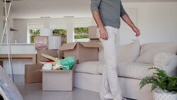 Man sits on sofa in living room surrounded by moving boxes Stock Footage