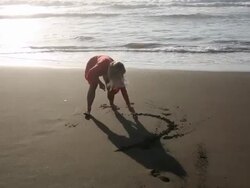 Woman hops onto beach, draws heart picture in sand Stock Footage