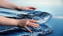 A woman uses her hands to create splashes in water leaving ripples and bubbles refelcted in a blue sky.  Stock Footage