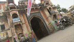 Traffic speeds past an old Moorish building decorated with an advertisement for bottled water on a balcony. Stock Footage
