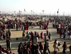 Crowds of colourfully dressed people criss cross large open sand covered space at the Kumbh Mela, India Stock Footage