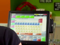 CU over shoulder of retail clerk at cash register entering a transaction into touch screen of point of sale computer and swiping a credit card to charge the amount of 8 dollars Stock Footage
