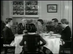 1941: WWII HOME FRONT: DRAMATIZATION: WS Davis home. INT House dining room w/ the Davis family eating dinner, father carving ham, CUs family members, youngest daughter 'Carol', daughter 'Jane', son 'Teddy', elder son 'Bill Jr.' in uniform.  Americana Instructional Video