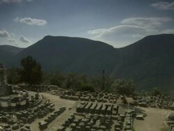 Wide Shot pan-left - Mountains tower in the background at the site of an ancient Greek temple. / Greece Stock Footage