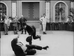B/W 1916 Charlie Chaplin as Little Tramp roller skating madly by man on floor Stock Footage