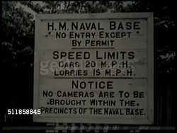 1938: SINGAPORE: British HM Naval Base sign w/ permit required, posted speed limits & notice for 'no cameras', sailors in shorts summer uniform carrying something on shoulders onto ship, HA Angled WS Unidentified docked ship w/ narrow port beyond. Instructional Video
