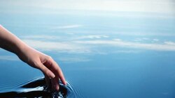 A woman uses her hand to create riples in water reflected in a blue sky.  Stock Footage