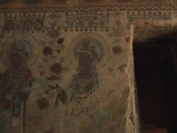 Inside a Sutra cave in China. Panorama of painted wall, then panning to a doorway and room exhibiting a Buddha statue.  Stock Footage