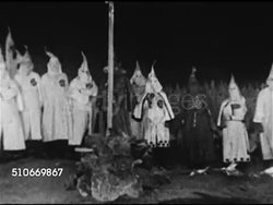 1920s: KU KLUX KLAN: KKK Klansmen in hooded robes standing next to burning cross (Grand Dragon or Imperial Wizard, leaders, in different color robe), Klansmen walking in line.   White Supremacists, supremacy, Racists, racism. Instructional Video