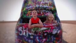 Young boy and young girl smile while peeking out of a graffiti painted Cadillac sticking out of the ground at Cadillac Ranch Stock Footage