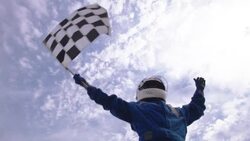 Woman in racing helmet waves checkered flag; blue racing team lifts woman up, celebrates stock car victory Stock Footage