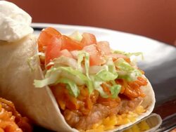 CU PAN across burrito on a plate with brown rice and beans as dollop of sour cream is spooned onto burrito Stock Footage