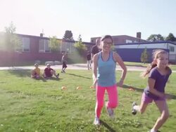 MS TS SLO MO Group of girls running race on grass field during athletics class with coach and classmates watching Stock Footage