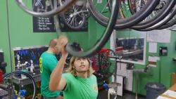 Shop employee grabs wheel and passes it to bike mechanic who attaches it to bicycle in busy repair shop Stock Footage