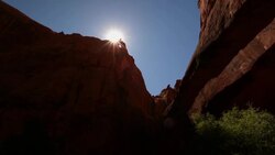 Sun shines at the tip of a rocky desert mountain summit with blue skies in Utah Stock Footage