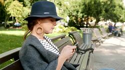 Beautiful young adult woman sitting on a bench in the city park and using her smart phone Stock Footage
