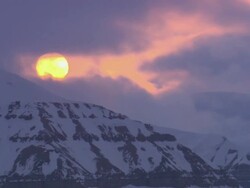 LA Clouds slowly enshrouding the sun as it's peeking over a snow-covered mountaintop / Svalbard, Norway Stock Footage