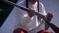 Older seated male Native American Indian holding and cleaning old rifle with cloth with teepee behind Stock Footage