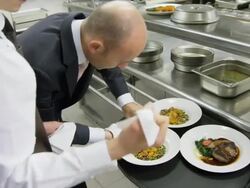 POV waiter taking prepared plates from the plating area in a restaurant kitchen to carry them to the dining room; camera precedes waiter into dining room Stock Footage