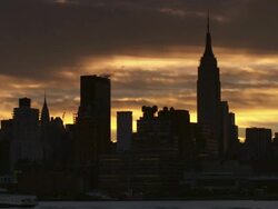Shot of the Midtown Manhattan skyline against a golden sky.  The Chrysler Building and Empire State Building are silhouetted against the sky. A boat goes along the Hudson River Stock Footage