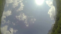 Wingsuit flier lands with parachute in mountain meadow Stock Footage