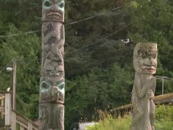 "CU pan of two thin totem poles in front lawn of wooden house in sunlight, Metlakatla, Annette Island, Alexander Archipelago, Alaska" Stock Footage