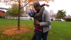 Couple in love embrace and kiss in autumn park with Brooklyn Bridge and New York skyline in background Stock Footage