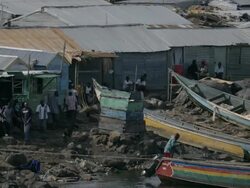 Tin houses, painted boats, people and pigs along rocky water edge Stock Footage