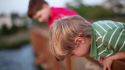 Young boys lean over dock railing, pull empty crab-trap out of river and toss it back in Stock Footage