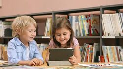 DS Boy and girl using a tablet sitting in library Stock Footage