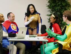 MS Dressing in superhero outfit, one woman standing at head of table while leading discussion with four other individuals also dressing in costumes with cape / Seattle, Washington, United States  Stock Footage