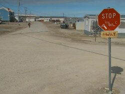 People travel the dirt road in the Arctic outpost town of Igloolik early summer.  Stop sign in Inuit Stock Footage
