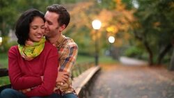 Young couple nuzzle on park-bench in Central Park, exchange kisses on the cheek (dolly-shot) Stock Footage