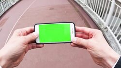 Man holding a smartphone with a green screen, while walking Stock Footage