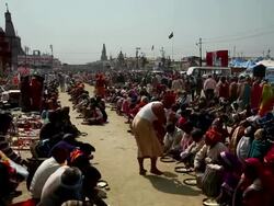 Hundreds of people sit on the ground in lines receiving and eating meals served by lunghi clad barefoot men with buckets of food. Kumbh Mela, India Stock Footage