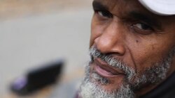 Old man in urban park stares at camera with saxophone case open for tips in background Stock Footage