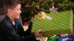 Young boy shakes present excitedly in front of Christmas tree Stock Footage
