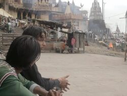 Two unidentified indian men chat outside a burning ghat near the Ganges river Stock Footage