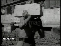 1950: YUGOSLAVIA CONSTRUCTION: HA WS Building construction. MS Silhouette of workers carrying cement mixer on high floor of incomplete building. MS Workers carrying cement blocks. WS Men & women lifting train rail. VS Unloading bricks from freight. Instructional Video