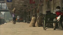 A pedestrian carries a head basket on a train platform near a sky bridge in India. Stock Footage