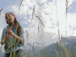 Girl holding grass in field below mountains Stock Footage