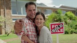 Portrait of happy couple holding keys in front of house with Sold sign Stock Footage