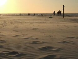 WS View of people walking on sea coast and sea sand flying by wind during sunset, North Sea North Frisia, / St. Peter Ording, Schleswig Holstein, Germany Stock Footage